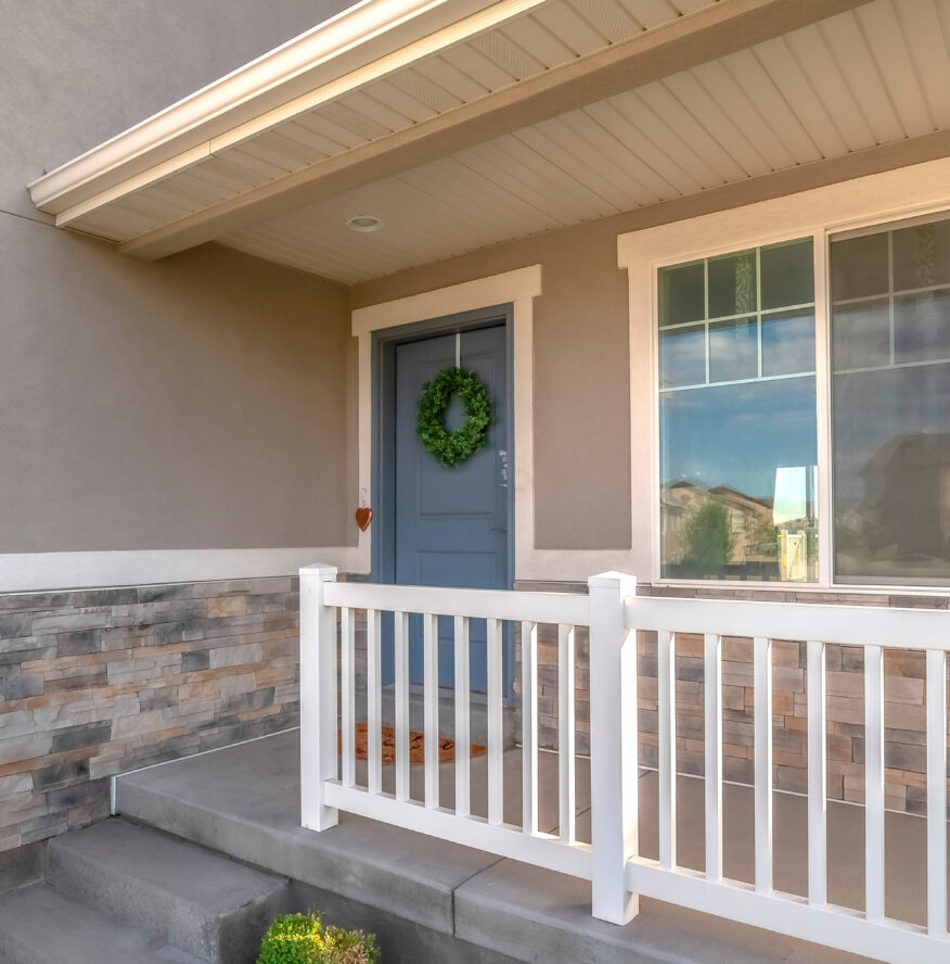 Pano Home facade with small porch and blue gray front door with green leafy wreath